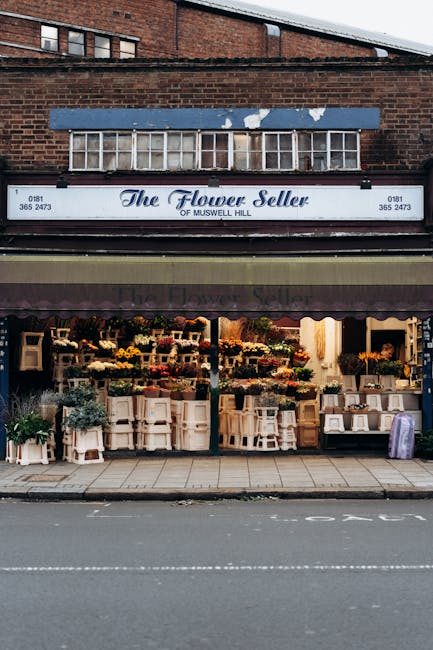 The storefront of The Flower Seller of Muswell Hill showcasing a vibrant display of fresh flowers arranged in bouquets and containers, with a variety of blooms including yellow, orange, pink, and purp