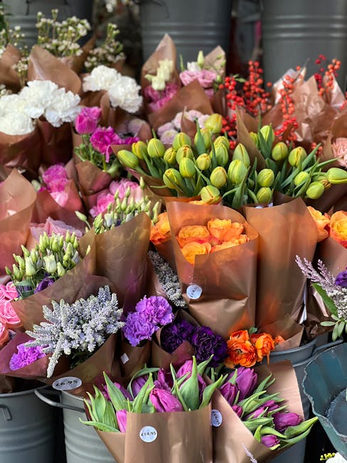 A vibrant display of fresh flowers arranged in brown craft paper wraps, including clusters of white hydrangeas, pink roses, purple lisianthus, green tulips, and red berries. The bouquets are set in me