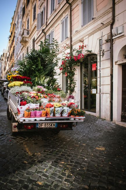 A delivery truck parked on a narrow cobblestone street in Islington, loaded with an assortment of fresh flowers and floral arrangements. The flowers include bright yellow sunflowers, white chrysanthem