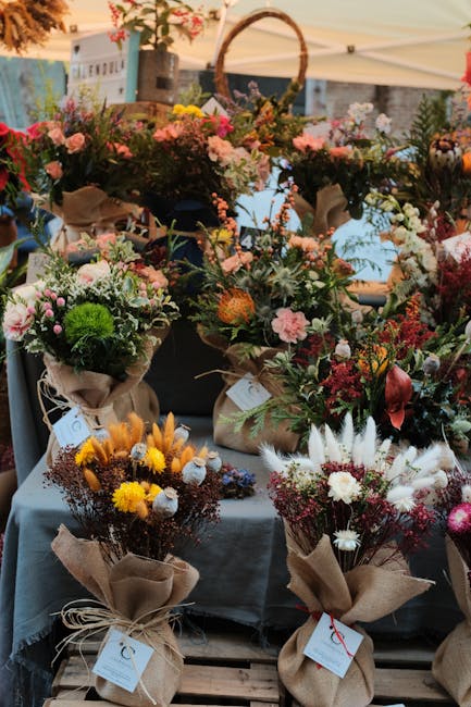 A display of various floral bouquets arranged on a table at an outdoor market stall, showcasing an assortment of fresh flowers including pink roses, white daisies, green chrysanthemums, and yellow bil